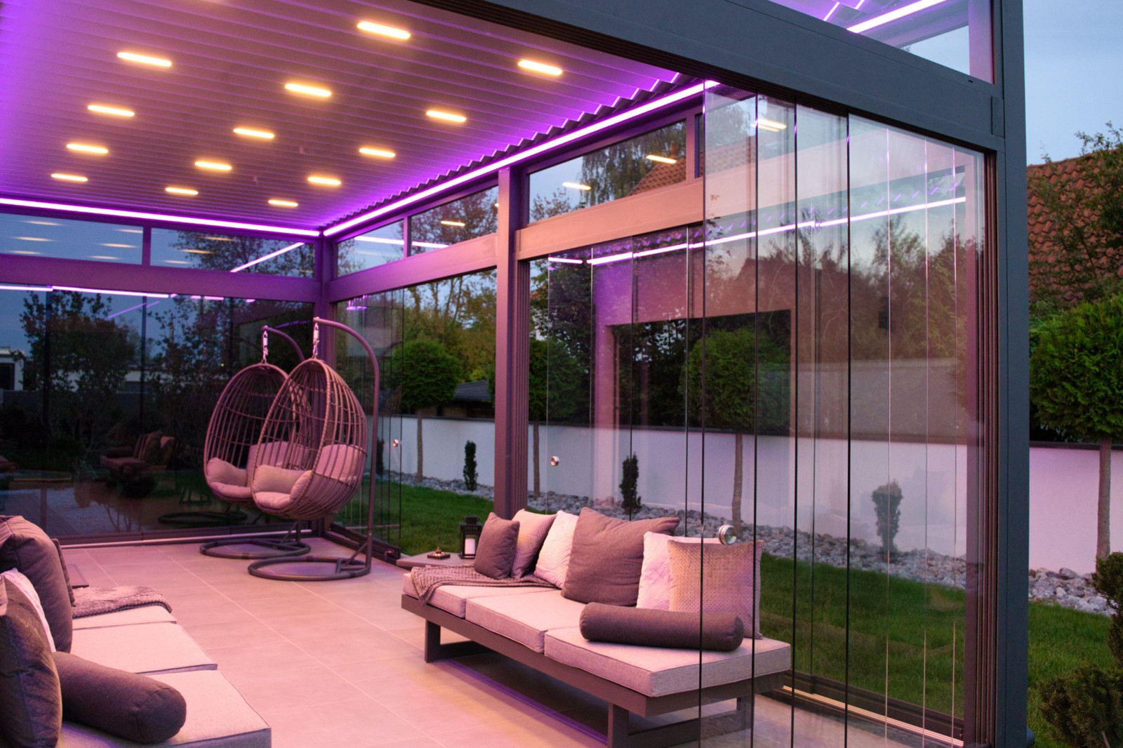 A patio adorned with purple lighting and chic furniture, creating a warm atmosphere under the pergola's integrated lights.